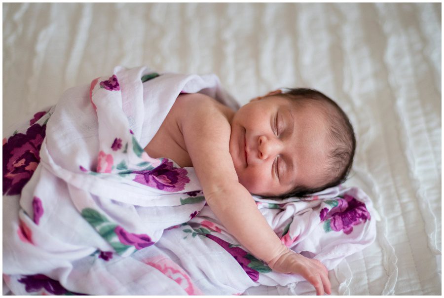 Newborn is wrapped in a swaddle and smiling while stretching.