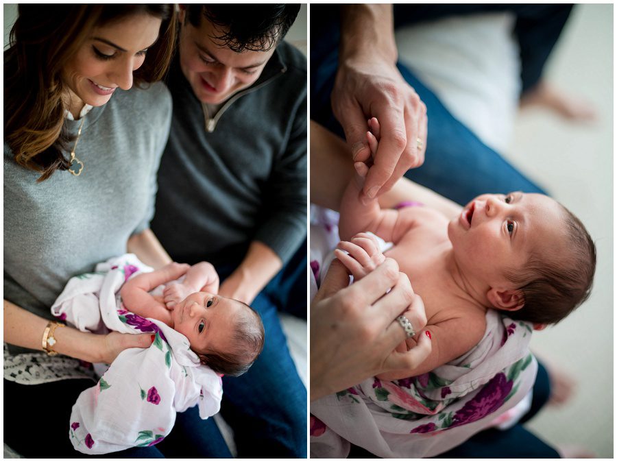 mother holding baby in home session on pink backless chairs vertical to parents holding sleeping newborn swaddled in blanket playing with newborn hands