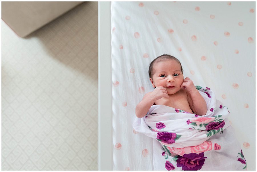 Newborn looks at camera and smiles as she lies in her crib in her nursery.