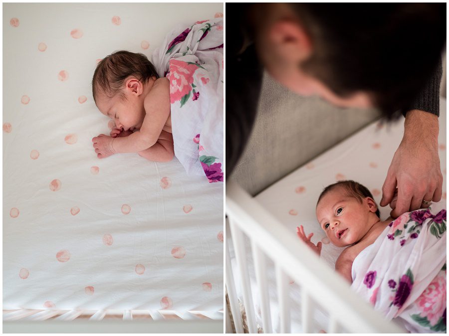 Newborn sleeping in her crib while wrapped in a swaddle. father is holding newborn's hand.