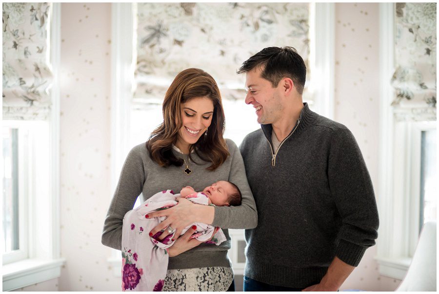 Mother is holding newborn in her arms as father smiles at his family.