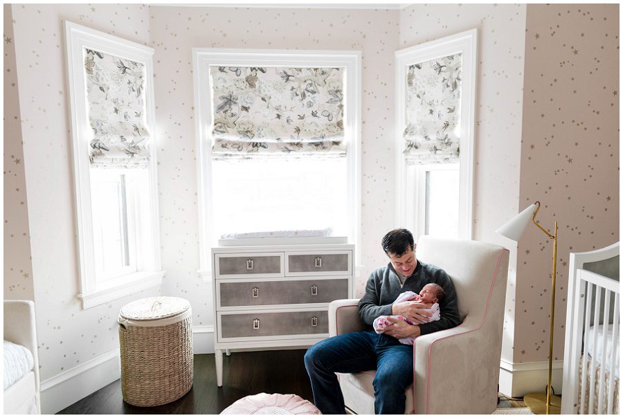 Father sits in a rocking chair while smiling at his newborn baby girl.