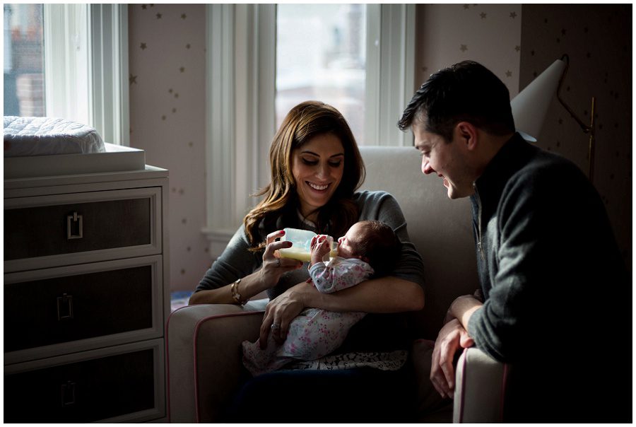 Mother feeding her newborn with a bottle as father looks on.