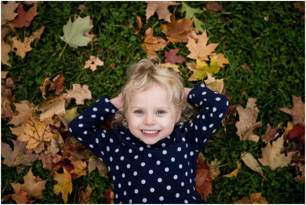 Child lying in leaves on ground Boston family photographer Fall foliage Larz Anderson