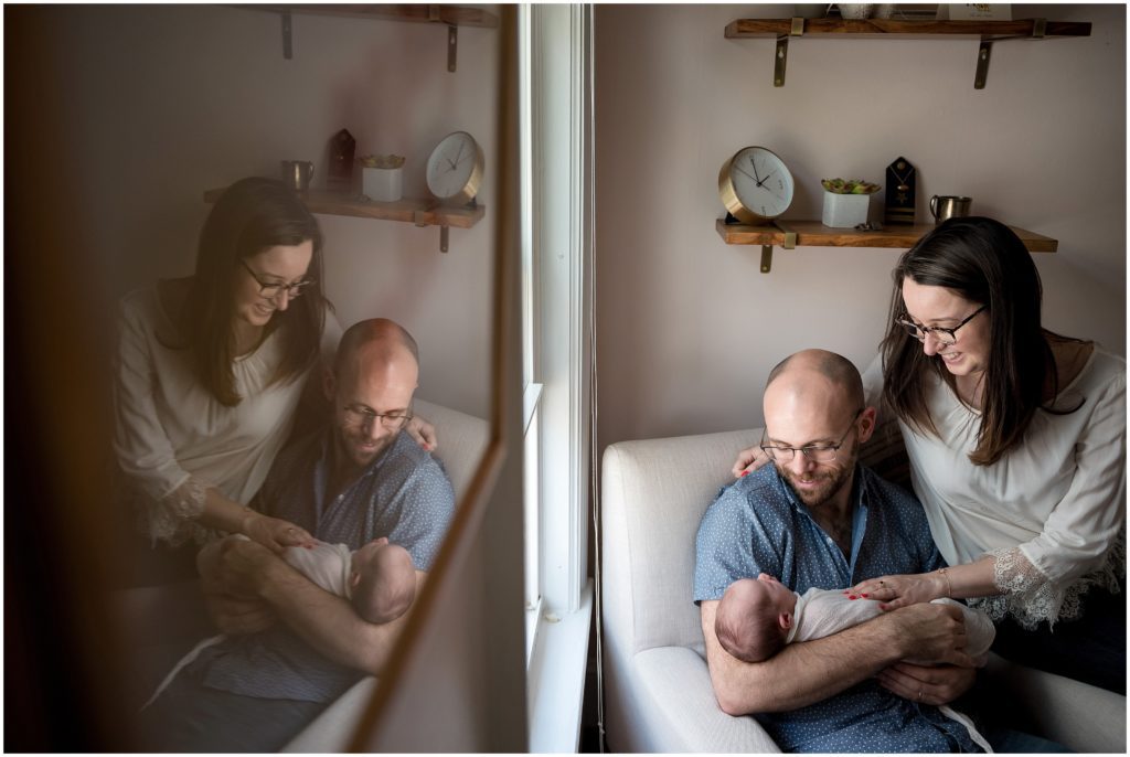 Dad holding daughter in nursery on rocking chair with mom hugging