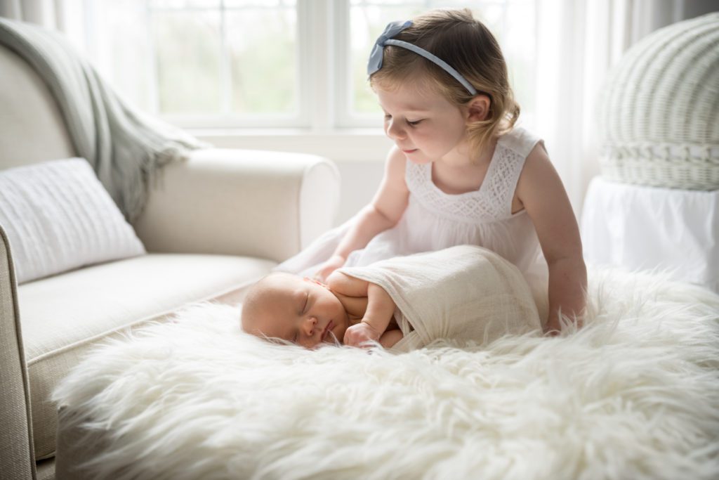 Side-lying newborn on ottoman with big sister