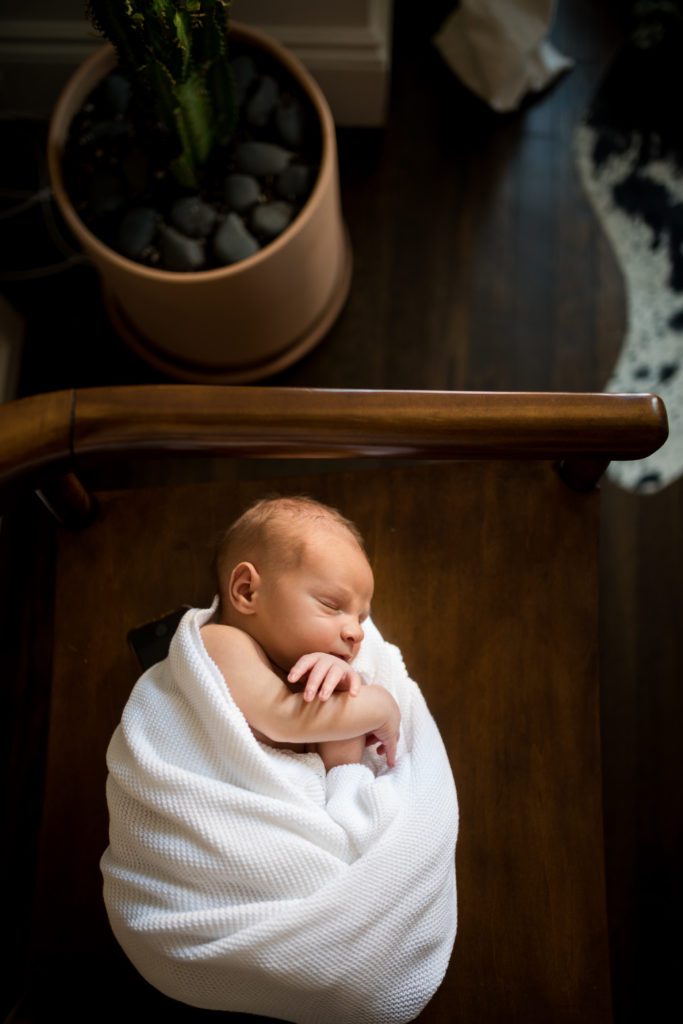 Side-lying newborn on chair by plant | newborn photos at home