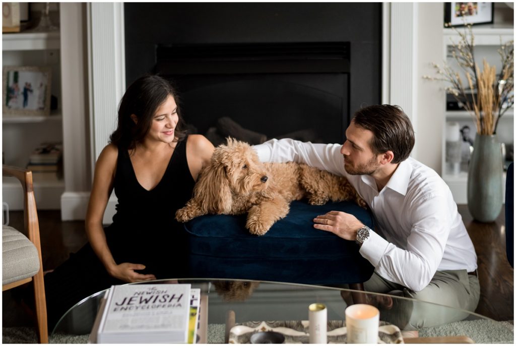snuggling their puppy at home in front of fireplace during maternity session