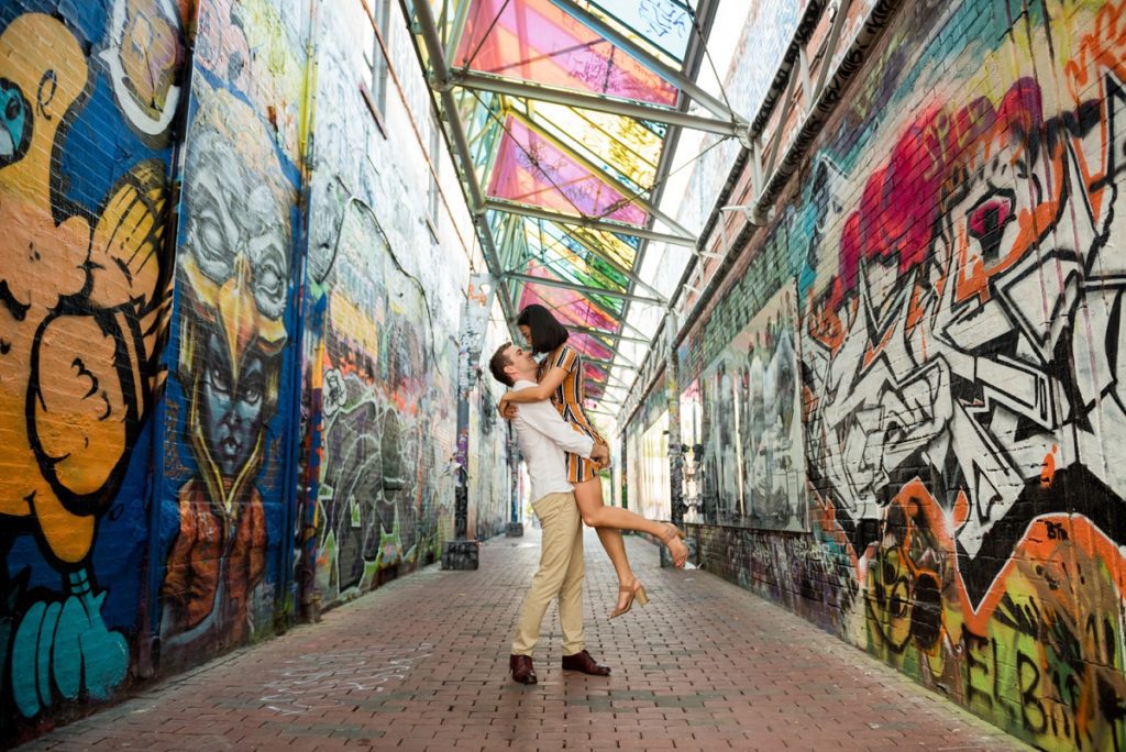 guy lifting fiance during engagement session pose in graffiti alley boston