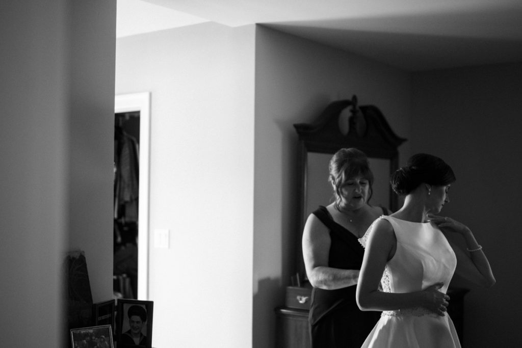 mother doing the back of the bride's dress in black and white image