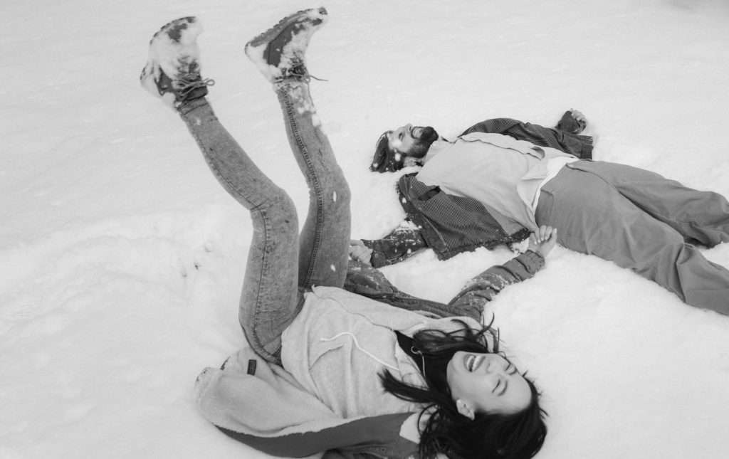 Couple lying in the snow together in Winter snow engagement