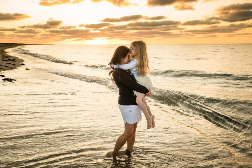 Child kissing mother's forehead in the ocean at Cape Cod